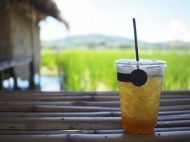 A glass of iced orange juice on bamboo table with rice fields and mountains background photo