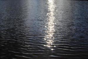 Detailed close up view on water surfaces with ripples and waves and the sunlight reflecting at the surface photo