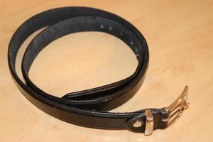 Slightly old black leather belt with a metal buckle on old wooden background photo