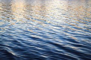 Detailed close up view on water surfaces with ripples and waves and the sunset sunlight reflecting photo