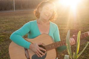 Happy Mature women playing and singing her acoustic guitar in the park photo