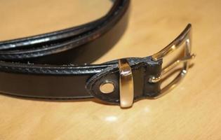 Slightly old black leather belt with a metal buckle on old wooden background photo