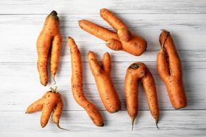 Ugly carrots lie on a light wooden surface photo