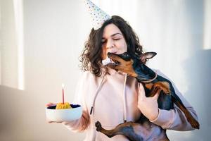 Happy young girl giving homemade cake to her dog, indoors photo