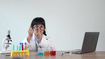 garota engraçada em óculos rindo com feliz, computador portátil e dispositivo de experimentar líquidos na mesa, enquanto estudava química científica, foco seletivo