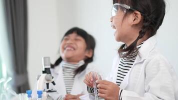 Slow motion shot, Two asian siblings wearing coat and clear glasses use microscope for experimenting with liquids, while studying science chemistry video