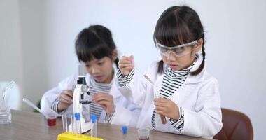 tir au ralenti, mise au point sélective, petite fille utilise un liquide compte-gouttes sur le test de la plaque, deux frères et sœurs asiatiques portant un manteau apprenant à expérimenter avec des liquides, tout en étudiant la chimie scientifique video