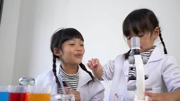 toma en cámara lenta, dos hermanos asiáticos con abrigo usando microscopio y lupa para experimentar con líquidos, mientras estudian química científica