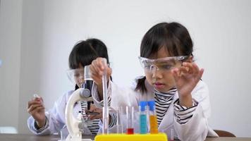 zwei asiatische geschwister in mantel und klarer brille benutzen das gerät zum experimentieren mit flüssigkeiten. während des Studiums der naturwissenschaftlichen Chemie video