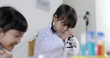 Selective focus, little girl use dropper liquid on plate test and looking in microscope, Two asian siblings wearing coat learning experimenting with liquids, while studying science chemistry video