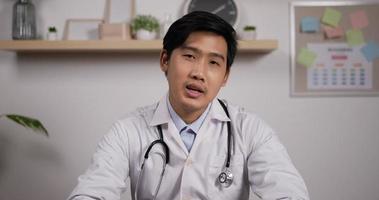 Portrait of young asian male doctor with stethoscope makes online video call consult patient and looks at camera. Medical assistant therapist videoconferencing. Telemedicine pandemic concept.