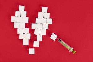 Broken heart made from sugar cubes and a syringe on a red background. Diabetes concept. View from above. Create space. photo