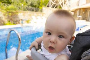 Handsome little boy sits in a baby carriage by the pool. Selective focus photo