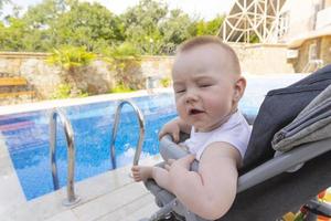 Handsome little boy sits in a baby carriage by the pool. Selective focus photo