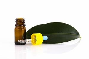 Blank amber glass essential oil bottle with pipette on green leaves background. Copy space photo