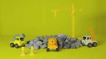 Stop-Motion auf gelbem Hintergrund, Baufahrzeuge, Spielzeug, Lastwagen, Bagger und Kräne arbeiten vor Ort, transportieren Ressourcenmaterialien, Felsen, Stein und Mörtel, gebautes Immobilienentwicklungsgeschäft. video