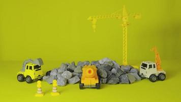 stop-motion sur fond jaune, jouets de véhicules de construction, camions, pelles rétrocaveuses et grues travaillent sur le site, transportent des matériaux de ressources, de la roche, de la pierre et du mortier, ont construit une entreprise de développement immobilier. video