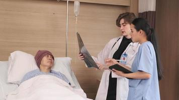 una doctora caucásica con diagnóstico uniforme explica la película de rayos X con un radiólogo asiático y un paciente varón en recuperación en la cama de una habitación para pacientes hospitalizados en una sala de hospital, clínica médica, consulta de examen de cáncer.