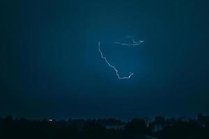 Lightning in sky over city. Bright flashes on dark night. Thunderclouds and electricity discharges in atmosphere. photo