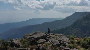 Luftdrohnenansicht, Rückansicht junger Wandermann, der mit glücklichen Händen auf dem Gipfel des felsigen Berges geht und sich erhebt video