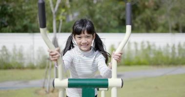 asiatische kleine Mädchen spielen gerne auf Outdoor-Trainingsgeräten mit einem Lächeln auf dem Spielplatz video