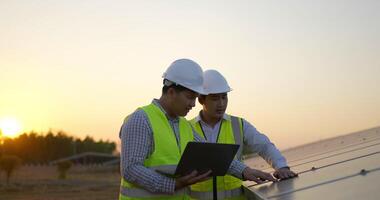 un ingénieur inspecteur asiatique et un jeune technicien utilisent un ordinateur portable, deux ingénieurs discutent et vérifient l'efficacité de la construction de panneaux solaires pour examen avec un ordinateur portable video