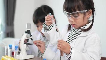 Slow motion shot, Two asian siblings wearing coat and clear glasses use microscope for experimenting with liquids, while studying science chemistry video