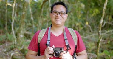 close-up, portret jonge toeristische man met casual kleding en bril met rugzak met digitale camera in handen glimlach en kijkend naar camera