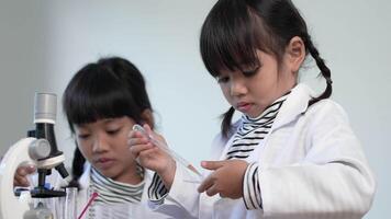 Slow motion shot, Selective focus, little girl use dropper liquid on plate test, Two asian siblings wearing coat learning experimenting with liquids, while studying science chemistry video