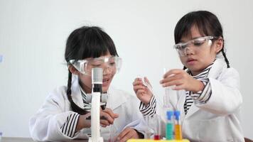 Slow motion shot, Two asian siblings wearing coat and clear glasses use microscope for experimenting with liquids, while studying science chemistry video