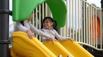 Cute older sister and youngest sitting talking and laugh with fun on the slider in playground video