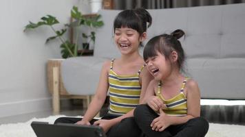irmã asiática sentada e se preparando para a pose de meditação, treinando em tablet na sala de estar, rindo com felicidade