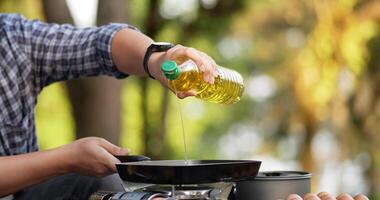 Nahaufnahme des Kochs, der Sonnenblumenöl in eine Pfanne gießt. Kochen im Freien, Reisen, Camping, Lifestyle-Konzept. video