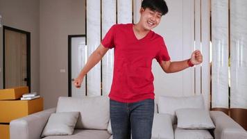 vrolijke aziatische jonge knappe man die danst in de woonkamer, hij vrijheid met danspasjes en lacht in de woonkamer bij een nieuw huis video