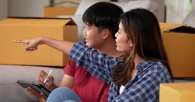 Slow motion shot, Young couple sitting front of sofa on floor and use tablet while counting boxs after relocation in their new home, new house concept video