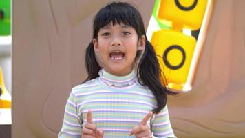zeitlupenaufnahme, porträt asiatisches süßes mädchen, das in der kamera steht, redet und lächelt mit glücklichem auf dem spielplatz video