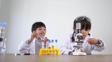 tir au ralenti, deux frères et sœurs asiatiques portant un manteau et des lunettes claires utilisent un microscope pour expérimenter avec des liquides, tout en étudiant la chimie scientifique video