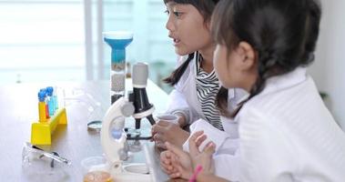 deux frères et sœurs asiatiques portant un manteau sur les genoux, une petite fille asiatique verse un liquide bleu dans une expérience de filtration de l'eau. étudier la chimie des sciences avec plaisir video