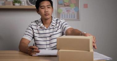 retrato de un joven empresario asiático que verifica la dirección del cliente en un paquete o paquete mientras está sentado en la oficina de su casa. concepto de comerciante en línea.