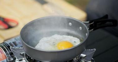 close-up de fritar um saboroso ovo frito em uma panela quente no acampamento. cozinhar ao ar livre, viajar, acampar, conceito de estilo de vida. video