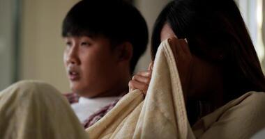 Selective focus, Asian young couple spend time watch scary movie on TV in living room in afternoon, Young man and woman sit on sofa and cover with blanket while watching television together video