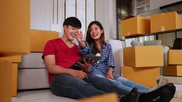 Slow motion shot, Young couple sitting front of sofa on floor and use tablet while checking boxs after relocation in their new home, new house concept video