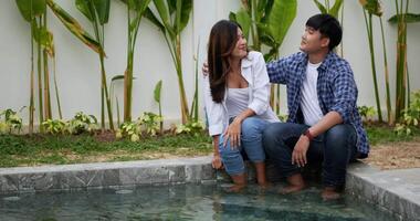 slow motion skott, asiatiskt ungt par njuter av att prata tillsammans i poolen i det nya hemmet, ung stilig man omfamnar axeln på frun, lyckligt familjekoncept video
