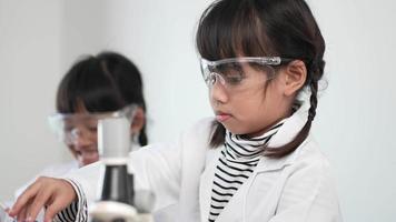 colpo al rallentatore, due fratelli asiatici che indossano cappotto e occhiali trasparenti usano il microscopio per sperimentare i liquidi, mentre studiano la chimica della scienza video