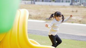 niña asiática jugando en el control deslizante y corriendo con felicidad en el patio de recreo video