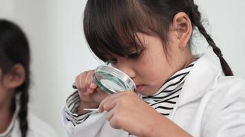 Slow motion shot, Selective focus, little girl use magnifying glass looking on plate test, Two asian siblings wearing coat learning experimenting with liquids, while studying science chemistry video