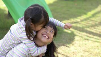 due sorelle asiatiche cavalcano sulla schiena della sorella maggiore e si baciano sulla guancia, si divertono insieme felici al parco giochi video