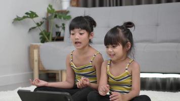 hermana asiática sentada y preparándose para la pose de meditación, entrenando en una tableta en la sala de estar, sonríe con felicidad video
