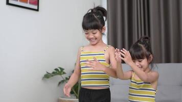 Sibling asian girl standing and preparing to meditation standing one leg pose, training on tablet in living room, laughing with happy video
