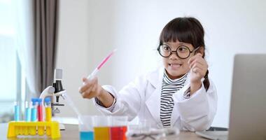 jolie fille à lunettes sourire avec plaisir, utiliser un microscope, un ordinateur portable et un appareil d'expérimentation de liquides sur table, tout en étudiant la chimie scientifique, mise au point sélective video